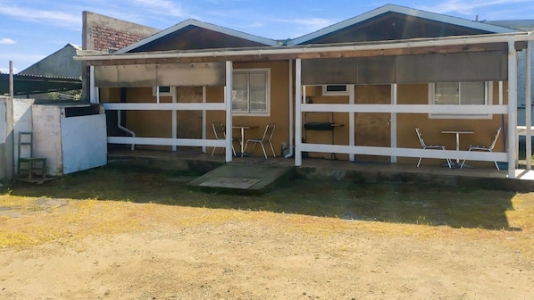 Un edificio de dos pisos con techo plano, un patio cubierto y un pequeño espacio con asientos al aire libre.