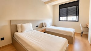 A bedroom with two beds, a desk, and a window with blinds. - New Listing (Agadir)