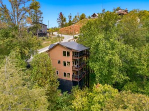 A multi-story building with a balcony on the upper floor, surrounded by dense trees. - Modern 4BR Cabin within minutes of Gatlinburg. Hot Tub! (Gatlinburg)
