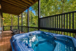 Ein Whirlpool unter einer Holzterrasse mit Metallgeländer, umgeben von Bäumen.