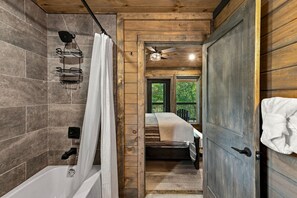 A wooden cabin bathroom with a shower, a bed, and a view of the outdoors. - Modern 4BR Cabin within minutes of Gatlinburg. Hot Tub! (Gatlinburg)