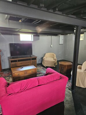 Una habitación con un sofá rosa, un aparador de madera, un televisor y un sillón color beige.