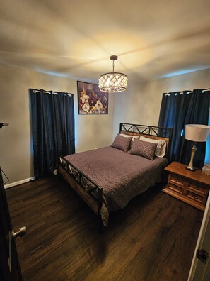 Un dormitorio con cama, mesita de noche, lámpara, ventilador de techo y un cuadro en la pared.