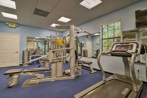 Een sportschool met trainingsapparatuur, een loopband en een vloerbedekt met blauw tapijt.