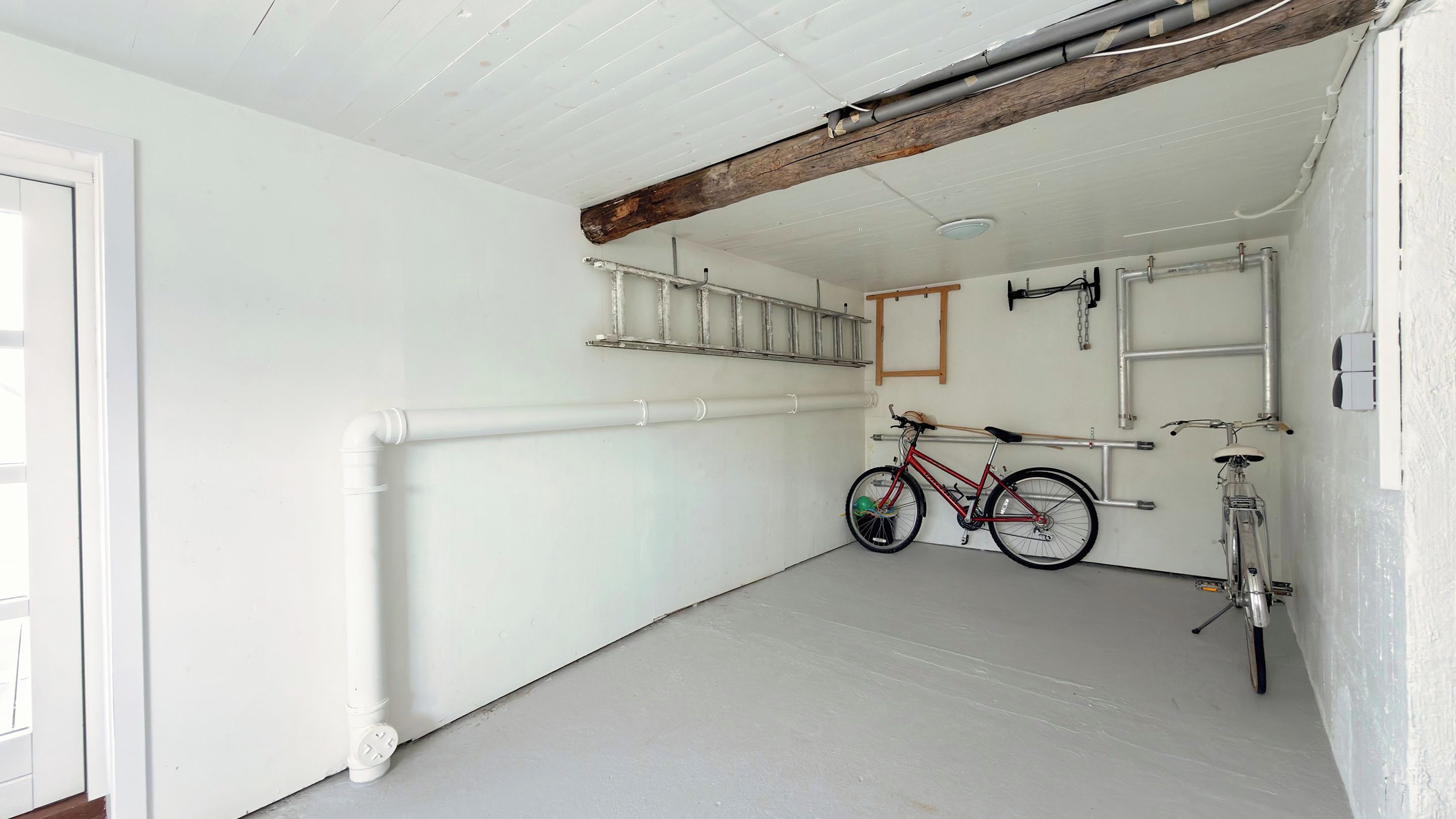 Una habitación limpia con paredes blancas, techo de vigas de madera, un aparcamiento para bicicletas y una puerta a la izquierda.