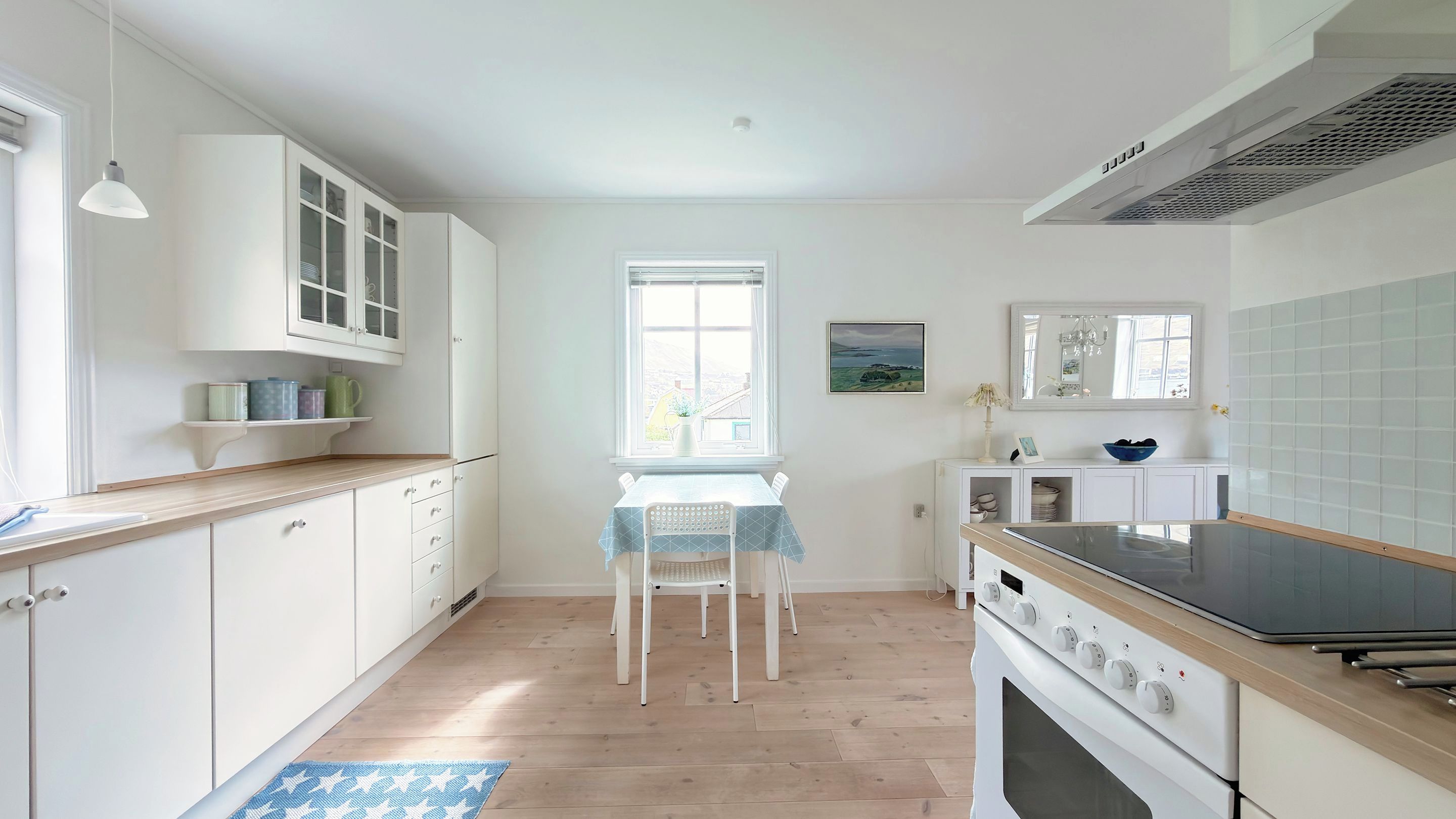 A kitchen with white cabinets, a dining table with chairs, a window, and a stove.