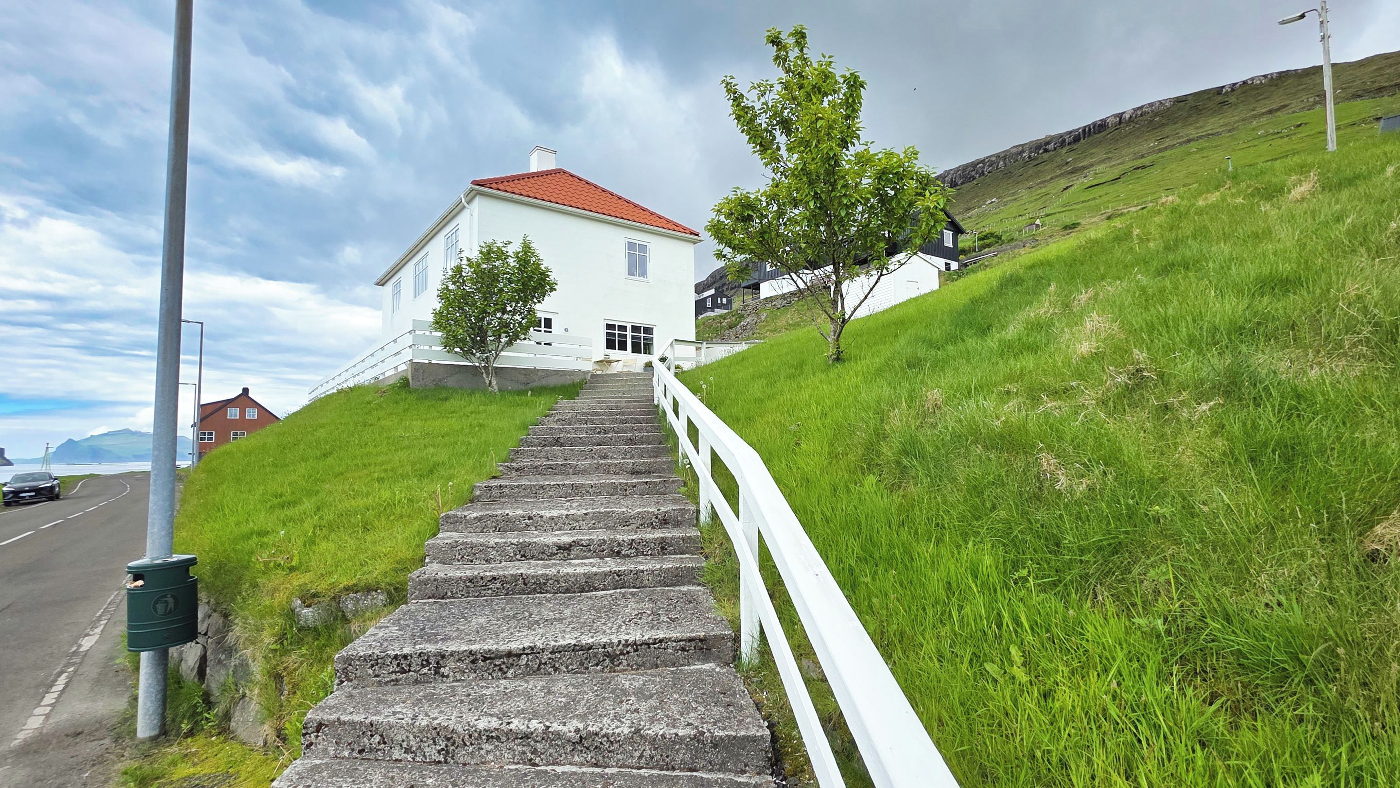 Ein weißes Gebäude mit rotem Dach, eine steinerne Treppe führt hinauf, und ein grasbewachsener Hang.