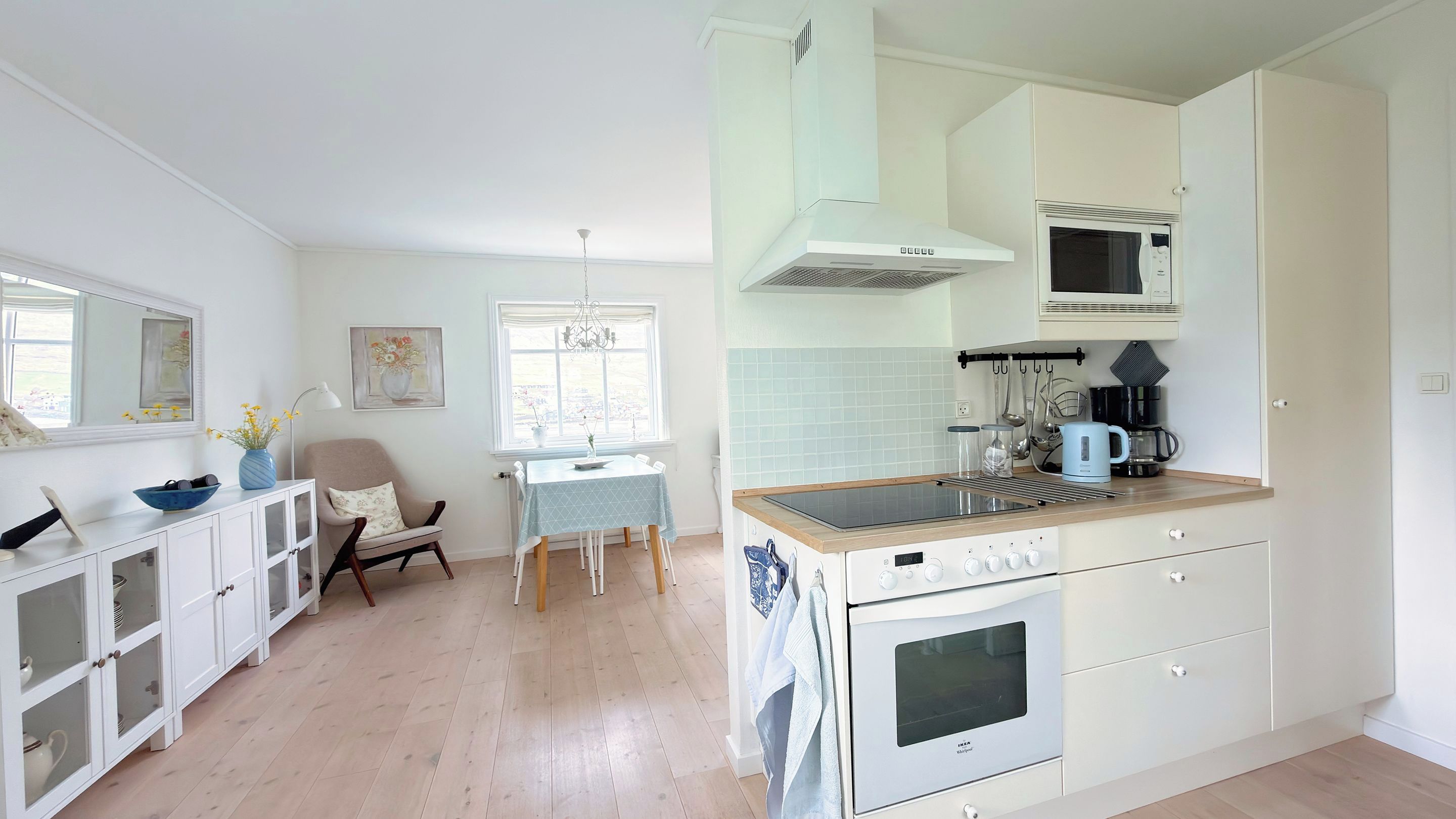 Una cocina moderna con armarios blancos, una isla central con estufa y una zona de comedor con mesa y sillas.