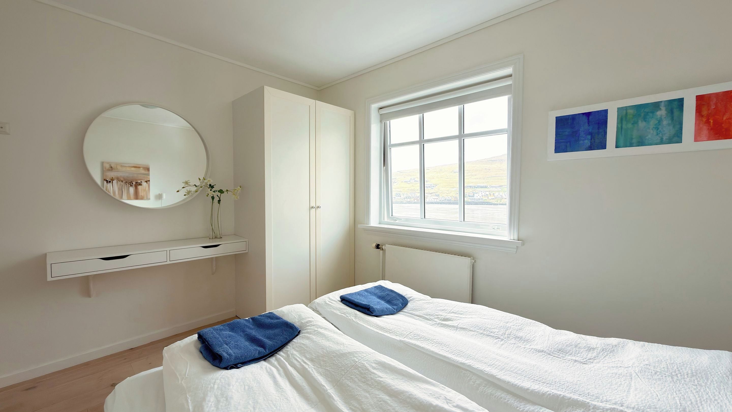 Ein Schlafzimmer mit Bett, Schrank, Spiegel und Fenster.