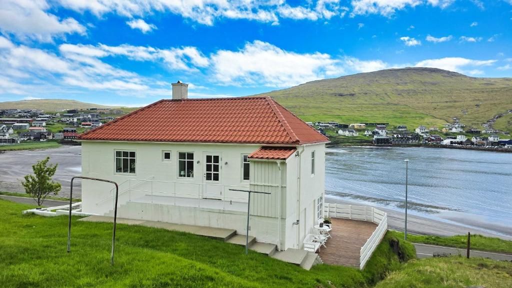 Een wit gebouw met een rood dak, gelegen aan het water, met uitzicht op een heuvelachtig landschap.