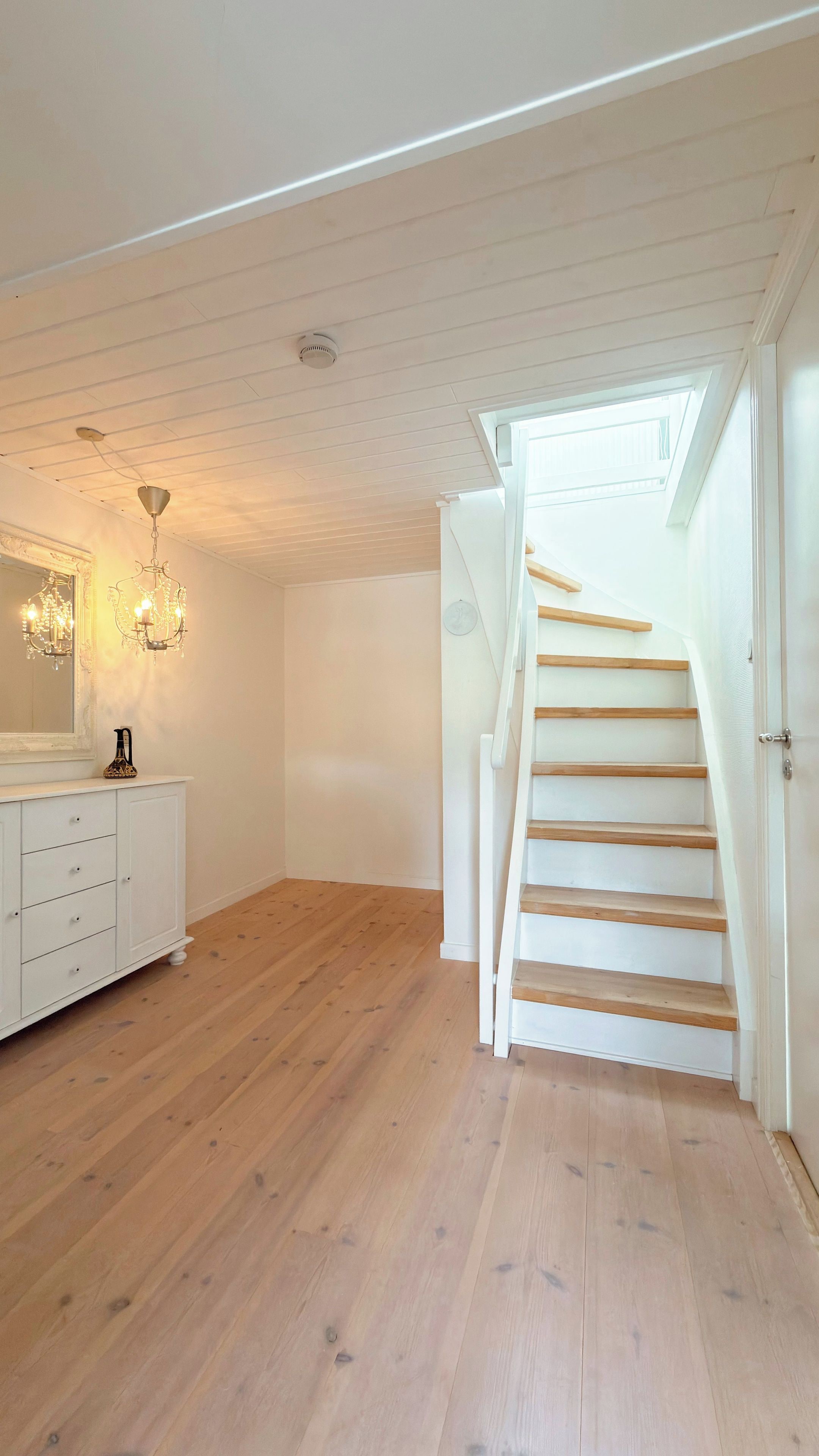 A spacious room with a wooden floor, a white staircase, and a white dresser with drawers.