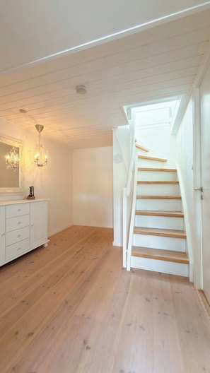 Una habitación amplia con piso de madera, una escalera blanca y un aparador blanco con cajones.
