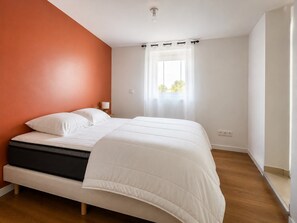 A bedroom with a bed, a window with curtains, and a wall with a different color.