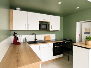 Een kleine keuken met witte kastjes, een magnetron, een koffiezetapparaat en een spoelbak.