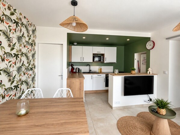 Een moderne keuken met witte kasten, een houten eettafel en een televisie erboven.