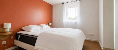 Chambre spacieuse et chaleureuse avec son mur terracotta signature. Grand lit douillet, fenêtre habillée d`un voilage laissant entrer une belle lumière naturelle en journée.