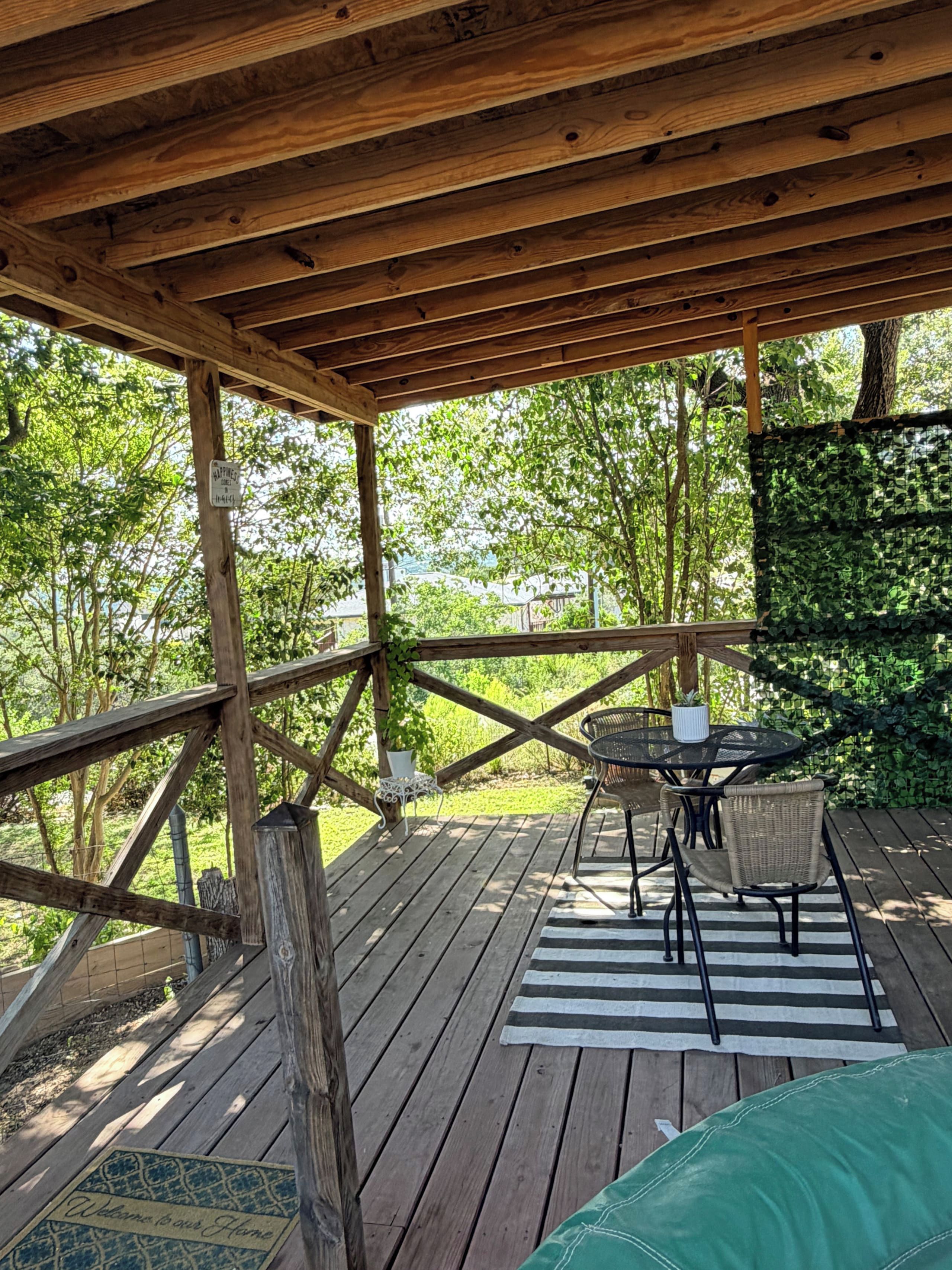 Een houten terras met een tafel en stoelen, omgeven door groen.