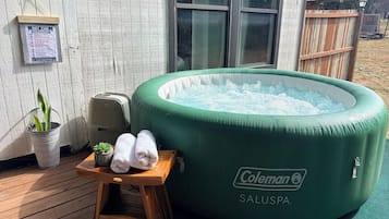 A green inflatable hot tub with a Coleman logo, a wooden stool with towels, and a metal bucket with plants.