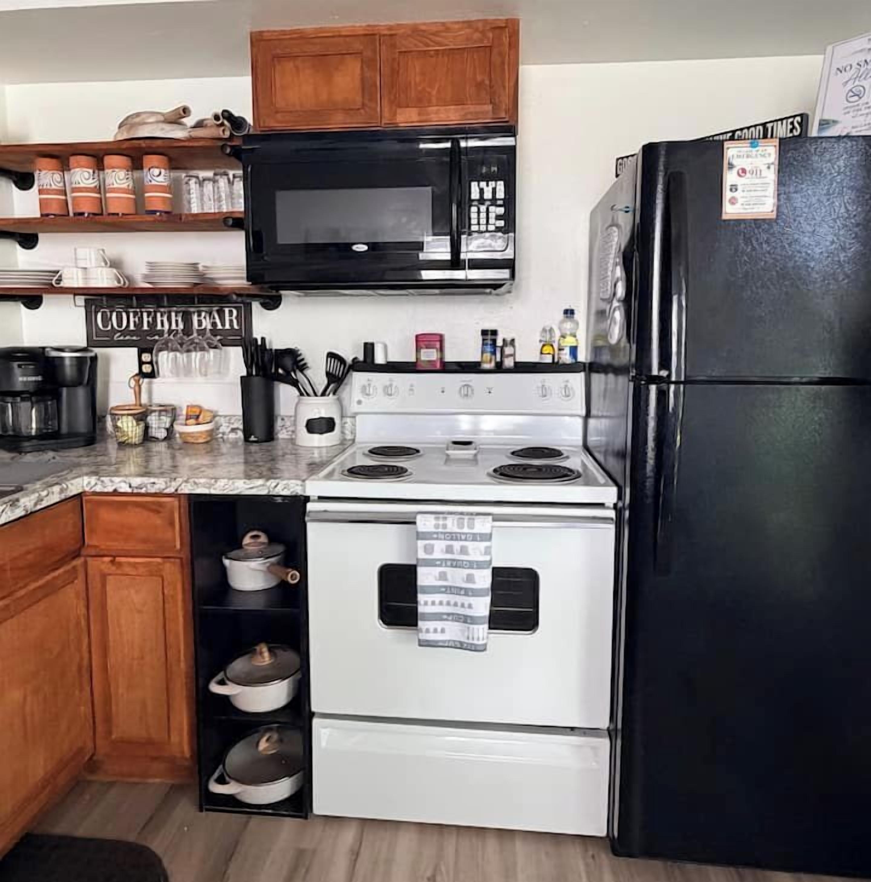 A kitchen with a stove, microwave, and refrigerator. There is a sign on the wall that reads 'COFFEE BAR.'