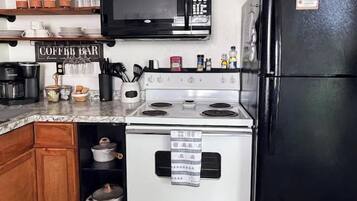 A kitchen with a stove, microwave, and refrigerator. There is a sign on the wall that reads 'COFFEE BAR.'