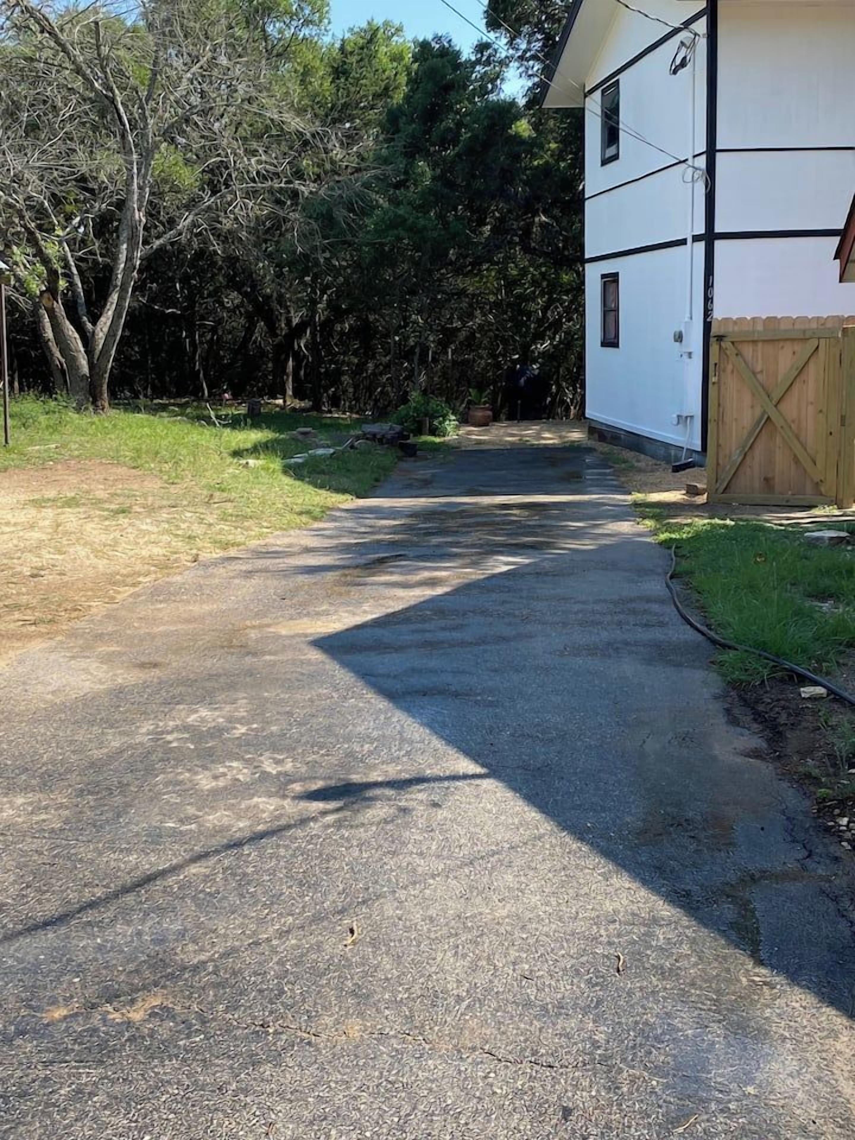 Un camino pavimentado que lleva a un edificio blanco con detalles negros, rodeado de árboles y una valla de madera.