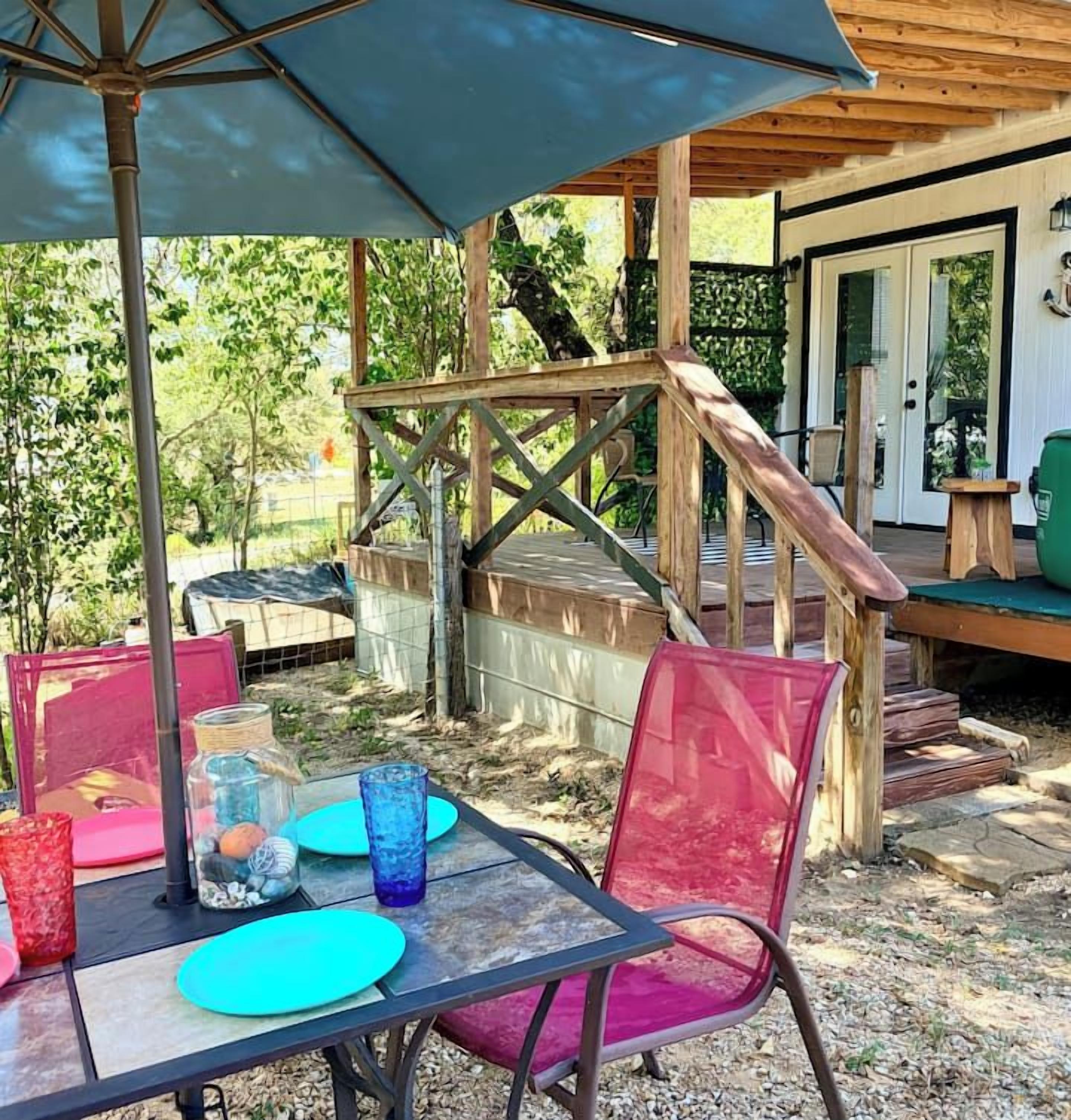 En udendørs terrasse med et bord, stole og en trætrap.