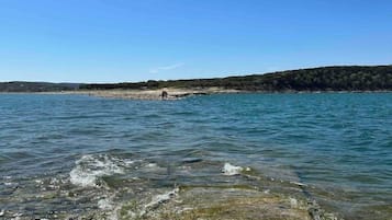 A clear view of a rocky shoreline with calm water, a distant sandy beach, and a forested hill in the background.