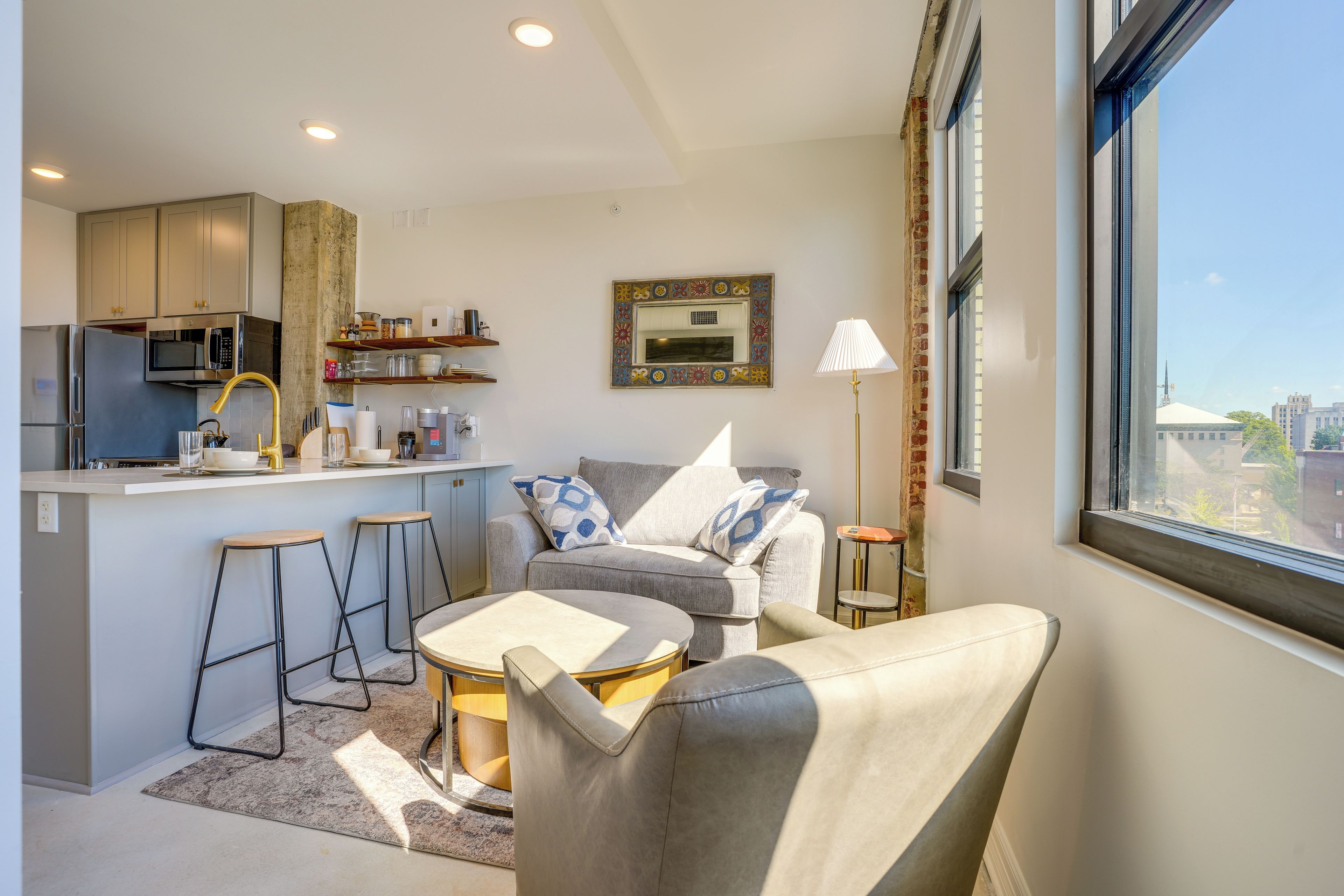 Un appartement moderne doté d’une cuisine, d’un coin salon et d’une grande fenêtre donnant sur la ville.