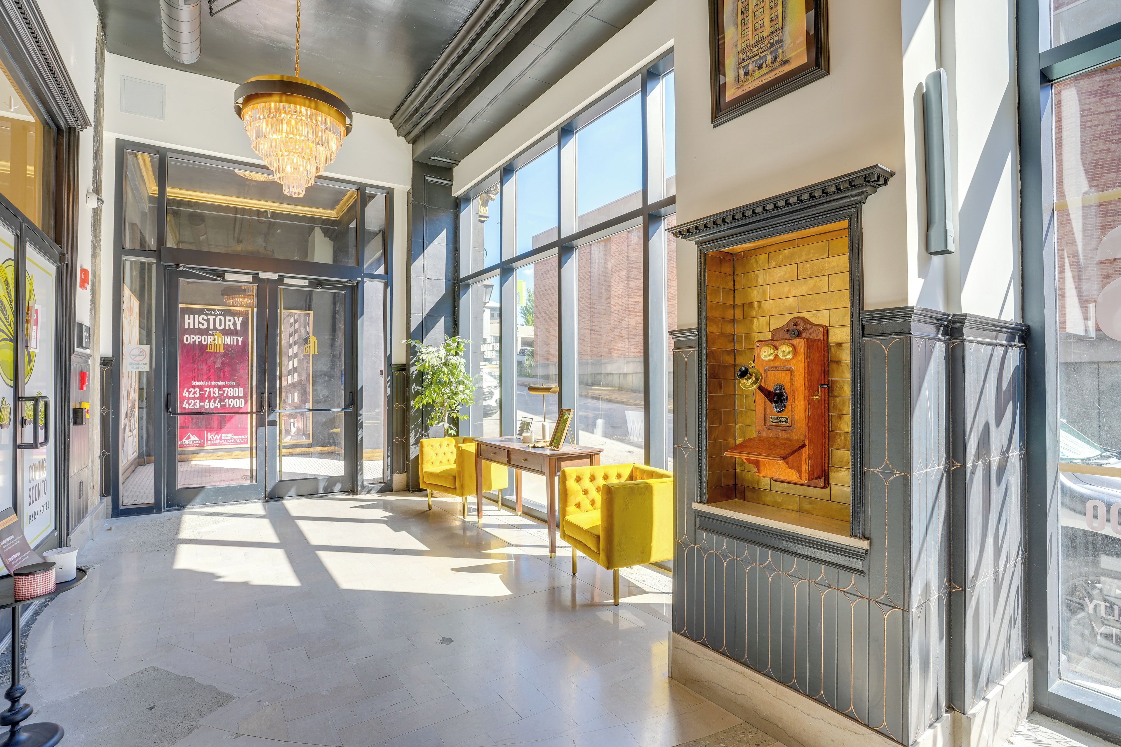A hotel lobby with a chandelier, a seating area with yellow chairs, and a large window with a view of the outside.