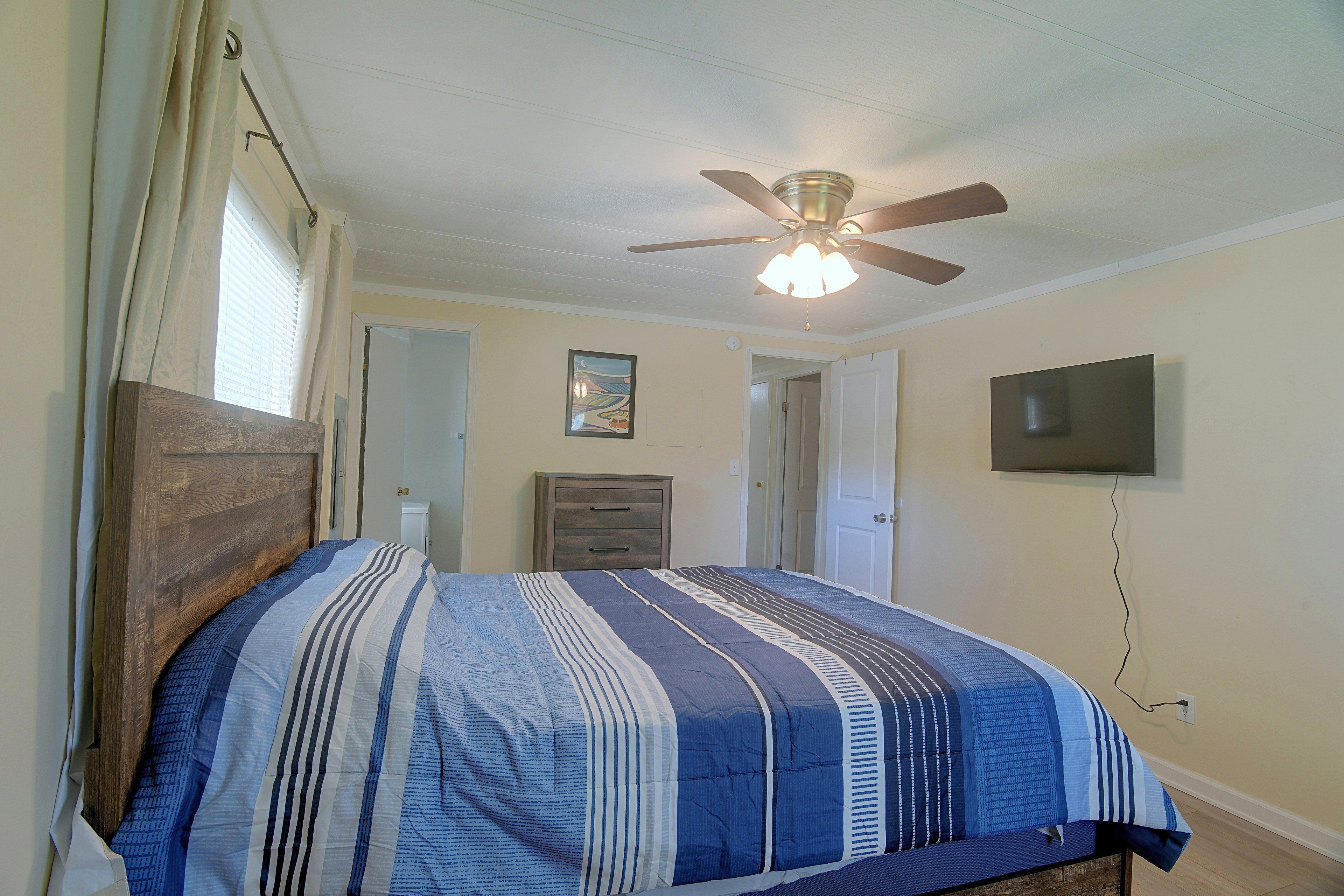 A bedroom with a bed, a ceiling fan, a television, and a door leading to another room.
