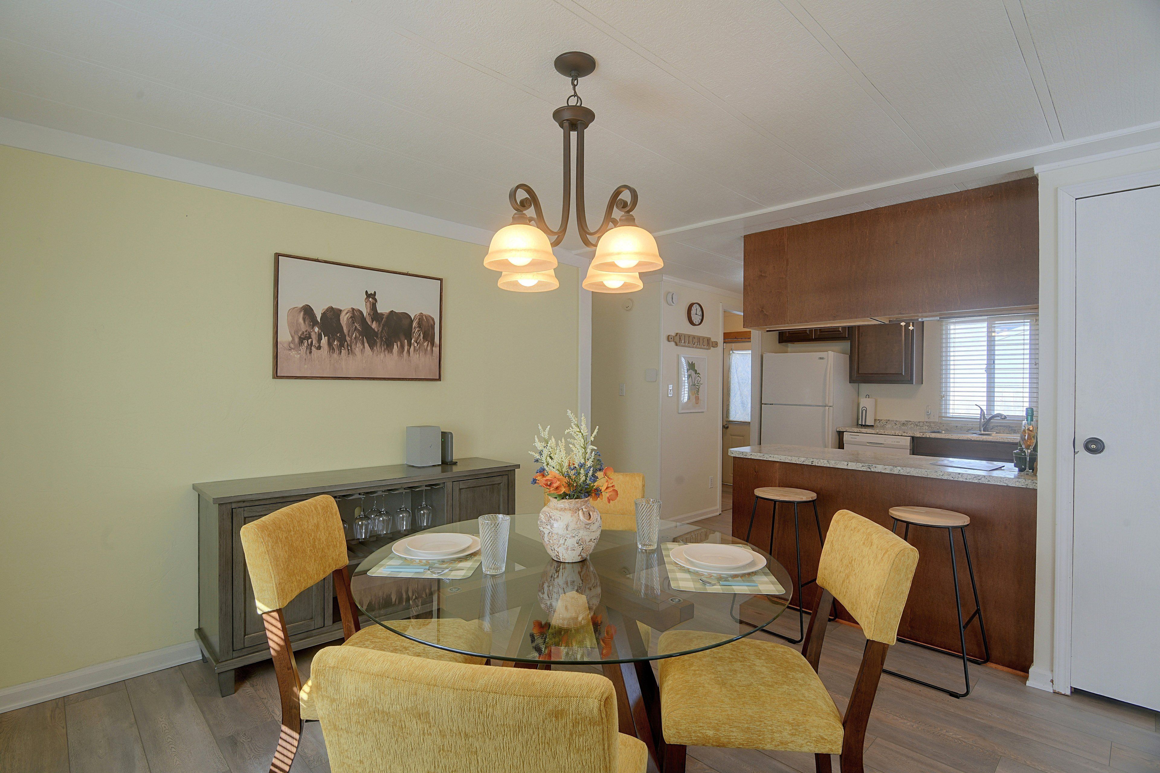 A dining area with a glass table, four chairs, a vase with flowers, and a painting on the wall.