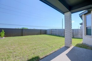 A backyard with a wooden fence, a concrete pillar, and a house with a window.