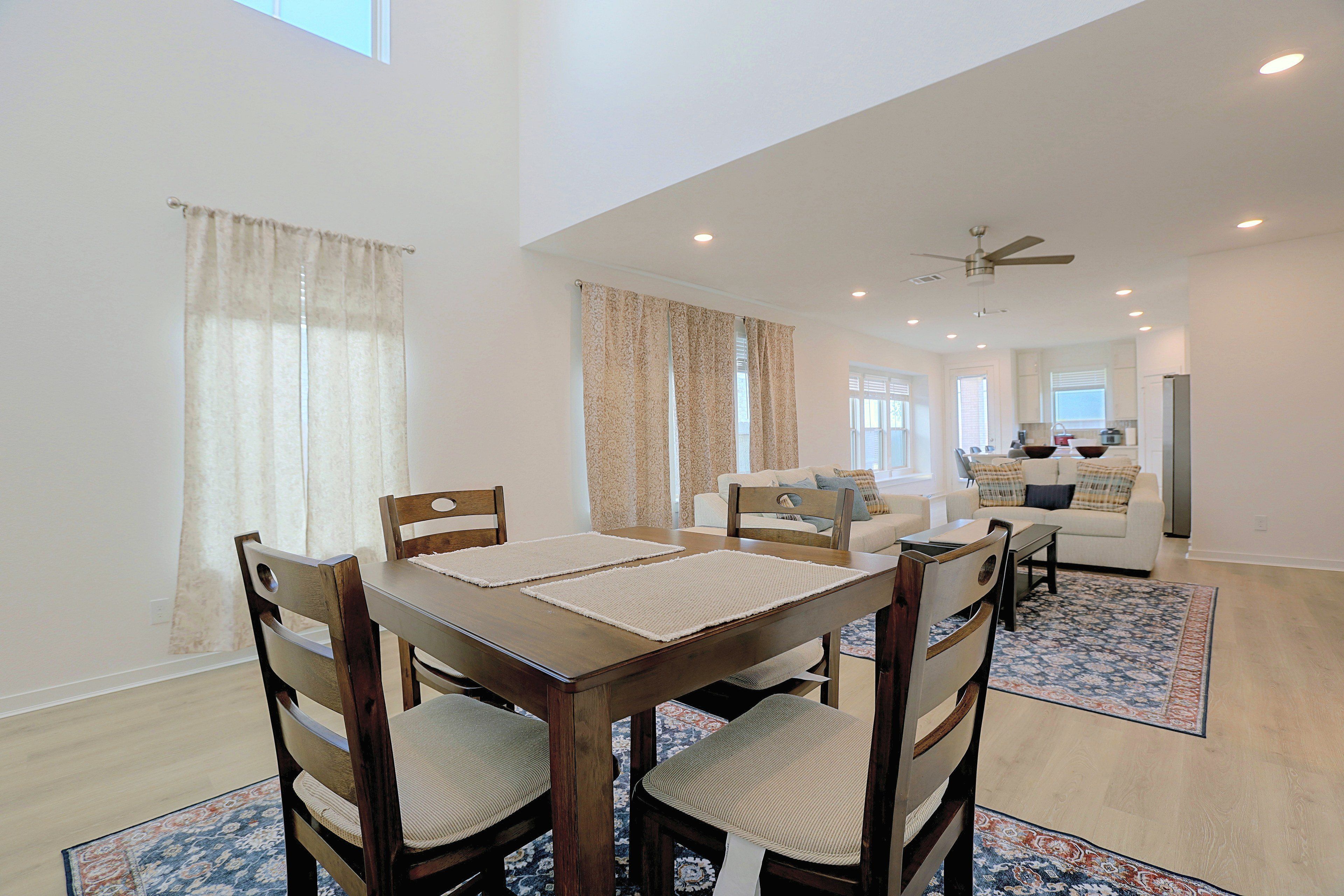 A dining area with a wooden table and chairs, a kitchen in the background, and a ceiling fan.