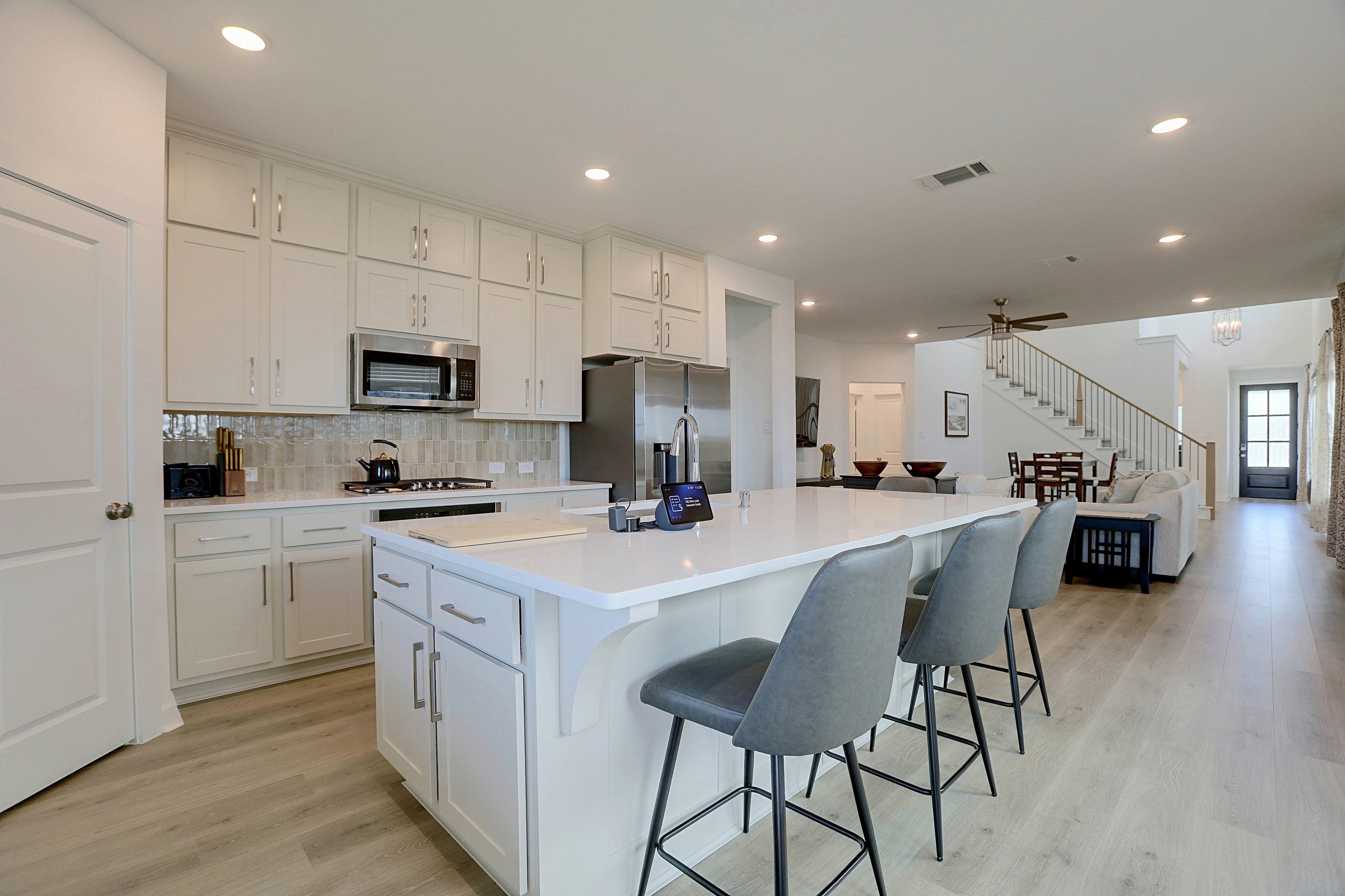 A modern kitchen with white cabinetry, a central island with bar stools, and a dining area with a staircase leading to another level.