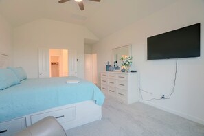 A bedroom with a bed, dresser, mirror, and a television mounted on the wall.