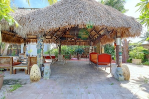 An outdoor seating area with thatched roof, wooden furniture, and stone lion statues. - Outdoor Oasis! Sprawling Miami Retreat Near Zoo (Miami)