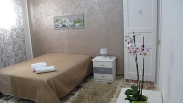A bedroom with a bed, a nightstand, a lamp, a painting, a door, and a potted plant.