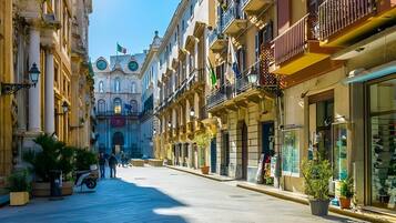 A street with buildings on both sides, a clear sky, and a few people walking.