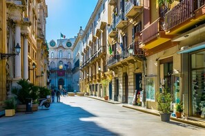 Una calle flanqueada por edificios, cielo despejado y algunas personas caminando.