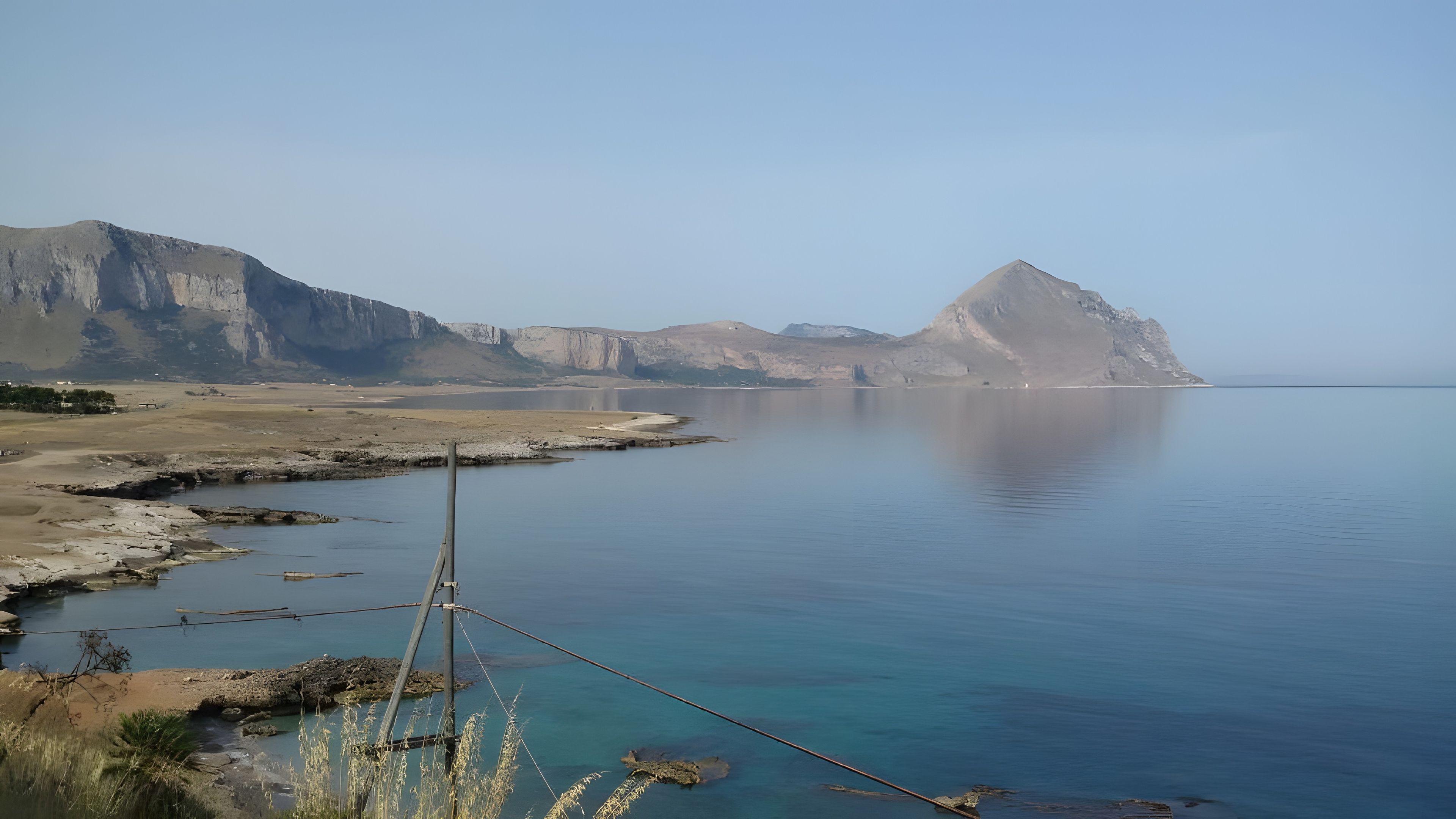 En rolig sø med et bjerglandskab i baggrunden og en fiskestang i forgrunden.