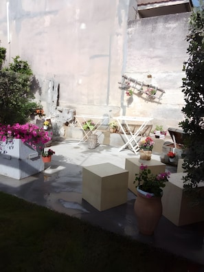 Un patio con mobiliario exterior, plantas en macetas y piso de concreto.