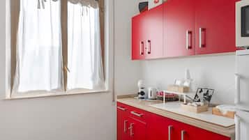 Eine Küche mit roten Schränken, einem Fenster mit weißen Vorhängen und verschiedenen Küchengeräten.