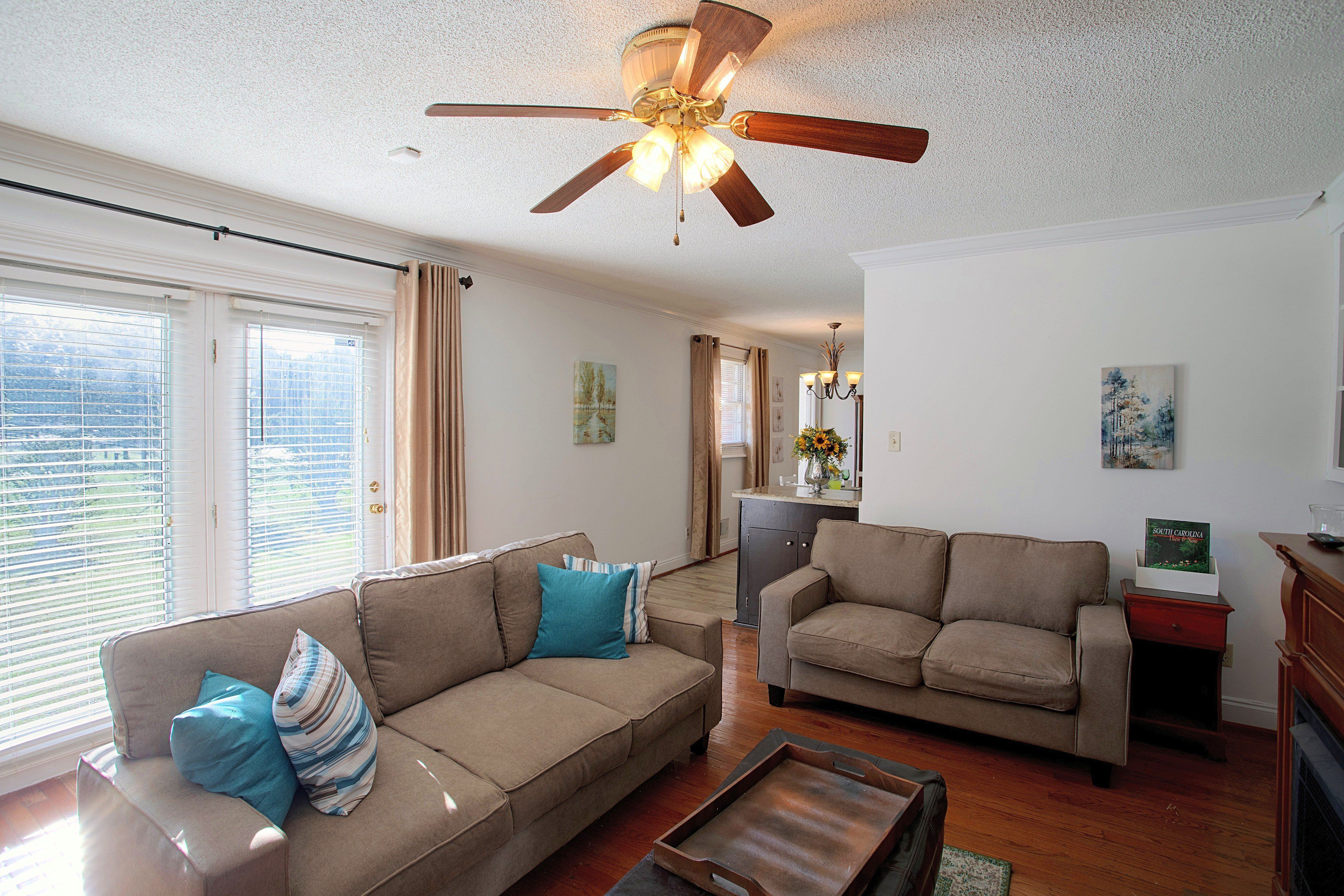 A living room with a ceiling fan, two sofas, a coffee table, and a kitchen area in the background.