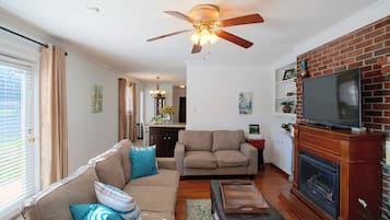 A living room with a sofa, armchairs, a television, a fireplace, and a ceiling fan.