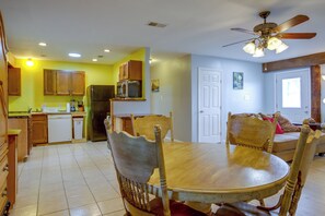 A dining area with a wooden table and chairs, a kitchen with wooden cabinets, a refrigerator, and a ceiling fan. - Your Home Base in Southern Louisiana (Buras-Triumph)