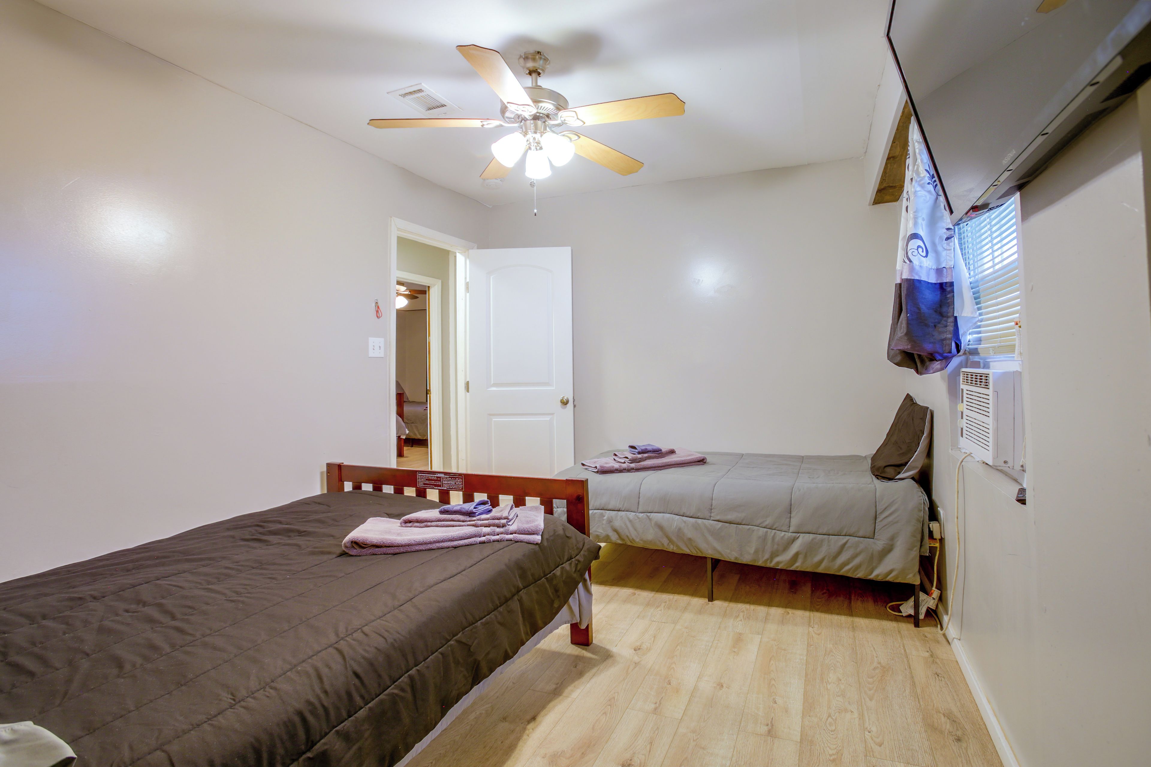 Un dormitorio con dos camas individuales, ventilador de techo, ventana con persianas y unidad de aire acondicionado montada en la pared.