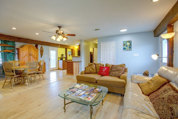 A spacious living area with a glass coffee table, a sofa with decorative pillows, a dining area with wooden chairs, and a kitchen in the background. - Your Home Base in Southern Louisiana (Buras-Triumph)