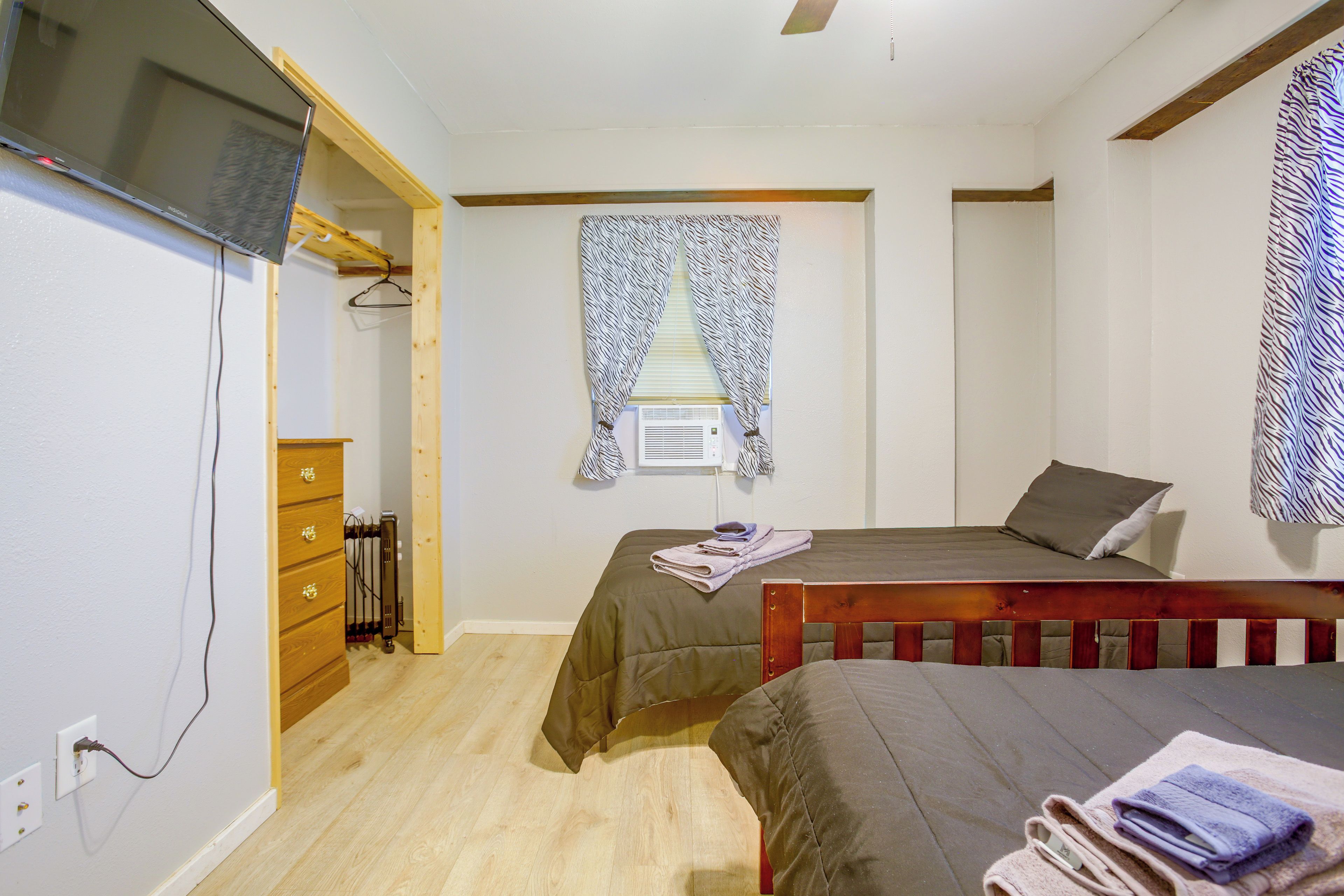 A bedroom with two beds, a wooden dresser, a TV, and a window with patterned curtains.