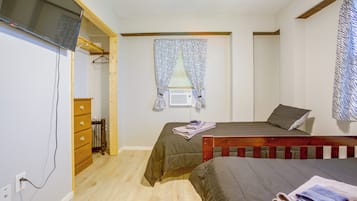 A bedroom with two beds, a wooden dresser, a TV, and a window with patterned curtains.