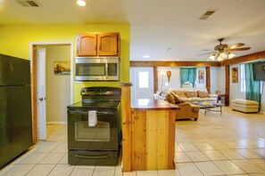 A kitchen with a refrigerator, oven, and microwave, a wooden island, and a living area with a sofa and a ceiling fan. - Your Home Base in Southern Louisiana (Buras-Triumph)